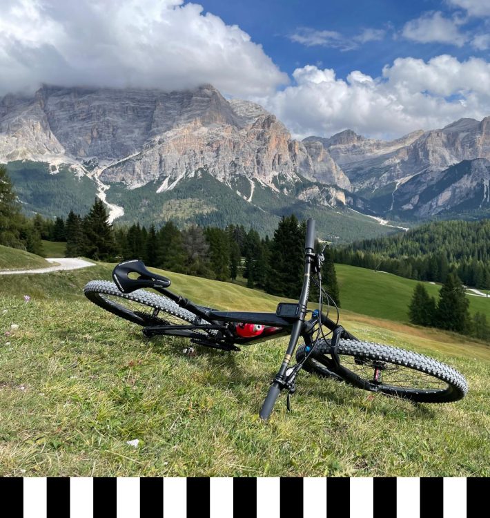 Trekking bike on a green meadow with a panoramic view of the Dolomites, a cloudy sky, and an alpine bike trail