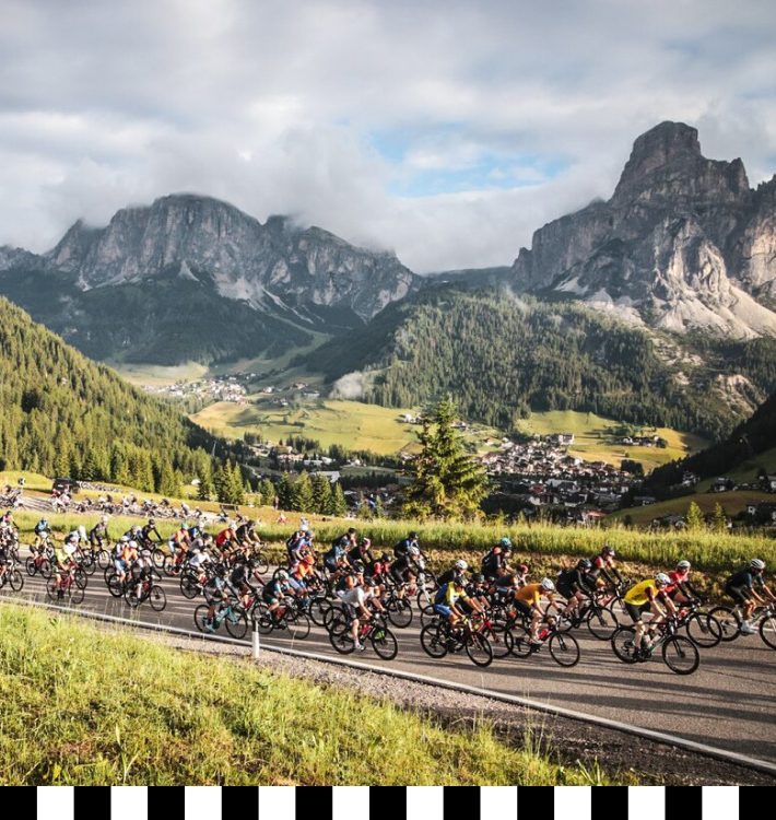 Cyclists competing in the 2024 Dolomites Marathon amid alpine landscapes, with the peaks of the Dolomites in the background