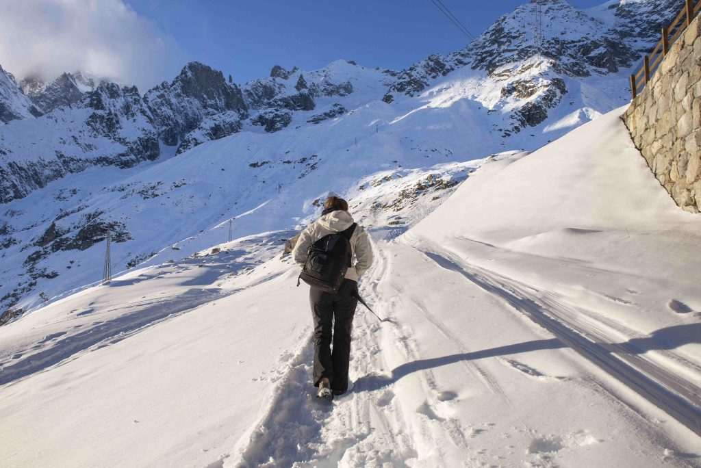 A person walking on a snow-covered mountain trail in winter; alternative activities to skiing; a sunny alpine landscape